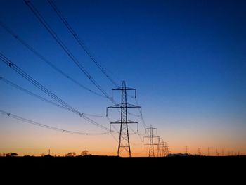 Low angle view of silhouette electricity pylons against clear sky