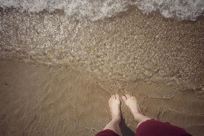 Low section of woman standing on sea shore at beach