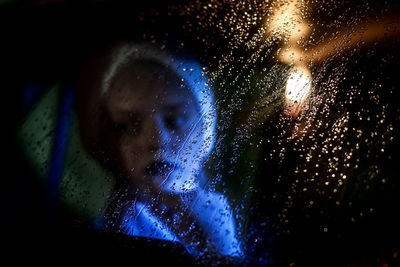 Girl sitting in car seen through wet glass