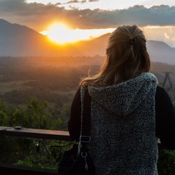 Rear view of woman looking at mountain against sky during sunset