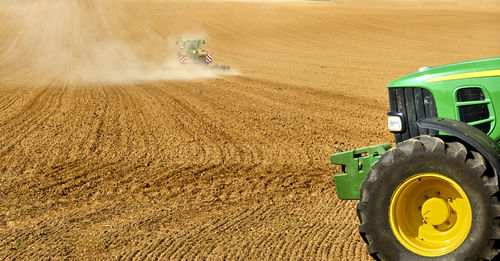 Tractor plowing a huge sandy empty field, with a second green tractor in the foreground