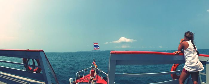 Rear view of woman standing on boat in sea against blue sky