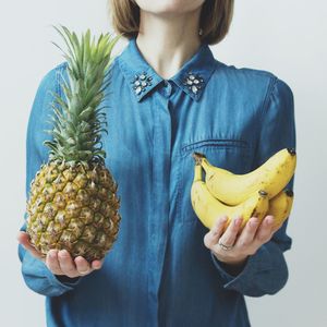 Midsection of woman holding pineapple and banana against white background