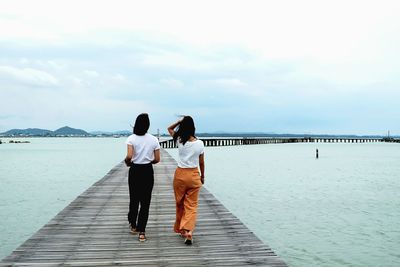 Rear view of friends walking on sea shore against sky