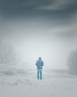 Rear view of man standing on snow covered landscape during snowfall