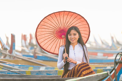 Portrait of smiling young woman holding umbrella standing outdoors