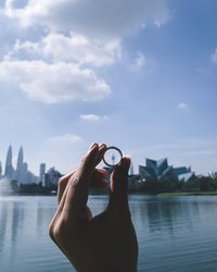 Cropped hand of person holding ring against sky