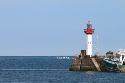 Lighthouse by sea against clear sky