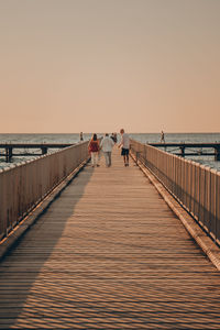 People walking by on pier against sky during sunset