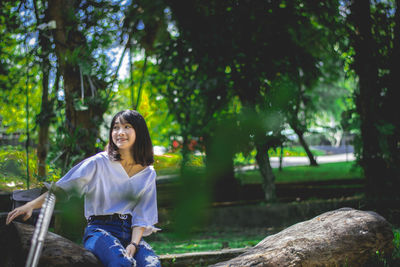 Young woman sitting on tree against plants