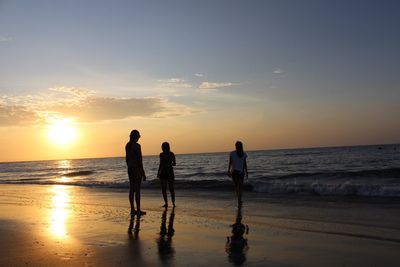 Silhouette people standing on beach against sky during sunset