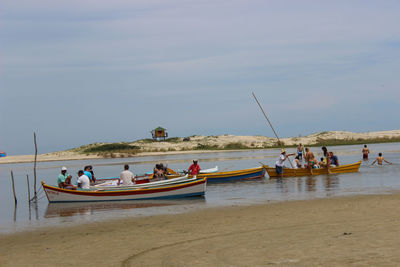 People with boats on shore at beach against sky