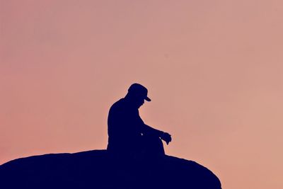 Silhouette man sitting on rock against sky during sunset