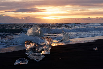 Snow covered land by sea against sky during sunset