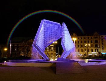 Illuminated bridge over street against buildings at night