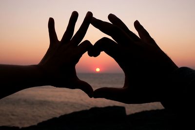 Cropped hands making heart shape against sky during sunset
