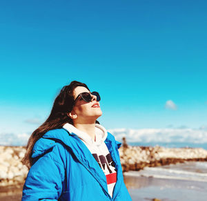 Portrait of young woman wearing sunglasses while standing against blue sky