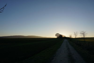 Road amidst field against clear sky during sunset