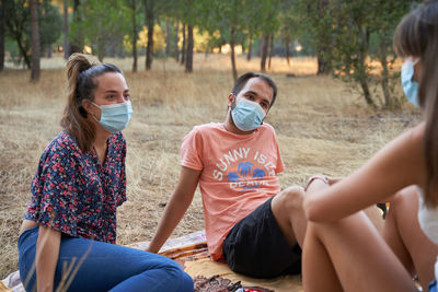 Friends wearing mask sitting in forest