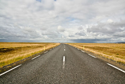 Empty road amidst field against cloudy sky