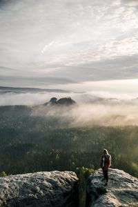 Man standing on rocks looking at mountain against sky