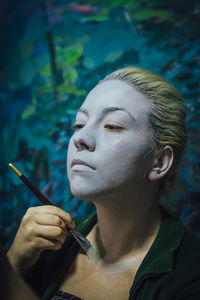 Close-up of young woman applying make-up in room