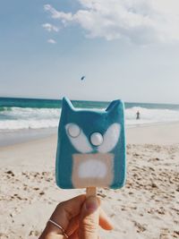 Close-up of hand holding ice cream at beach against sky