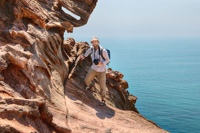 Man with camera on rock formation against sea and sky