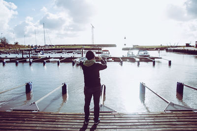 Rear view of man standing on pier at harbor