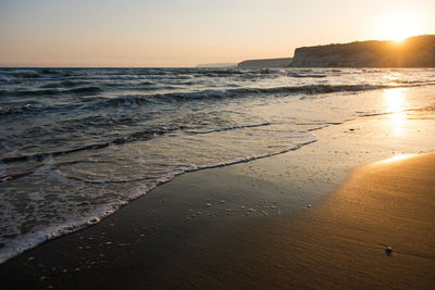Waves approaching beach sand during golden sunset