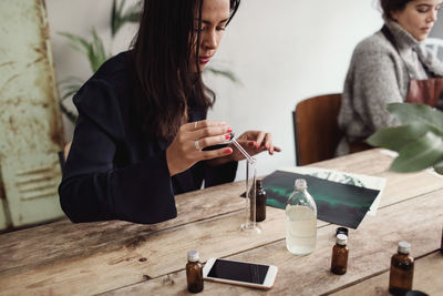 Mid adult woman mixing liquid with pipette in test tube at table in perfume workshop