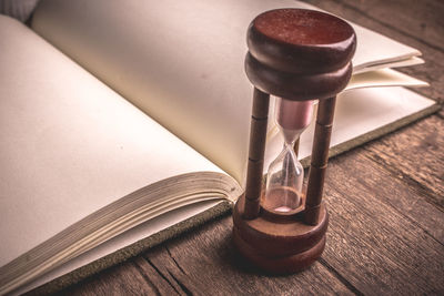 Close-up of hourglass by open blank book on wooden table