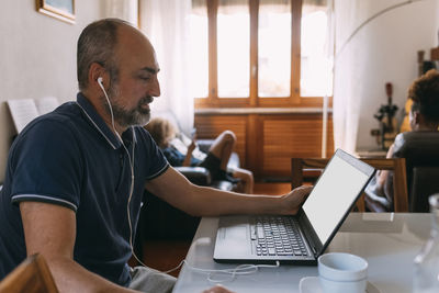 Businessman wearing in-ear headphones doing video call through laptop at home