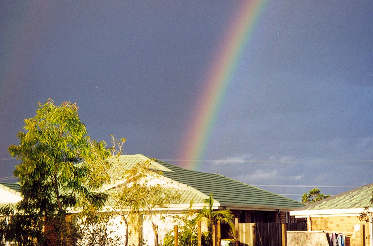 rainbow, sky, tree, scenics, low angle view, built structure, multi colored, beauty in nature, tranquility, architecture, nature, tranquil scene, cloud - sky, blue, idyllic, outdoors, building exterior, no people, house, cloud