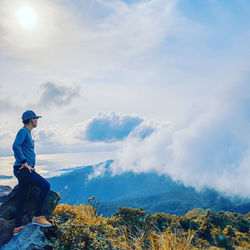 Side view of young man looking at waterfall against sky