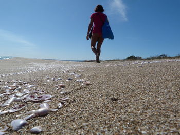 Rear view of woman walking on sand at beach against sky