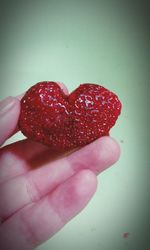 Close-up of hand holding red heart shape over white background