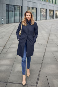 Portrait of smiling mature woman walking street against building