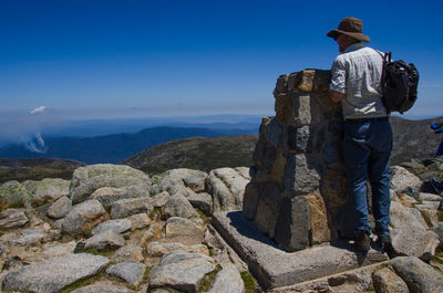 Rear view of man standing on rock against sky