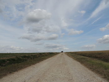 Dirt road amidst field against sky