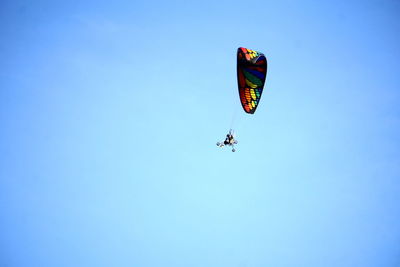 Low angle view of people paragliding against clear blue sky