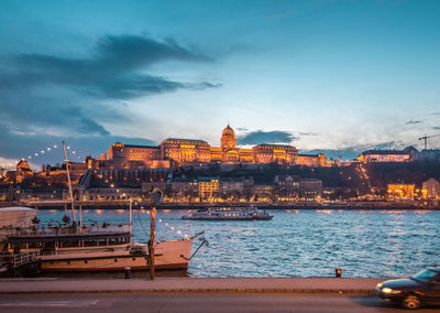 Boats moored on sea by city against sky during sunset