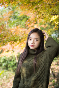 Portrait of young woman standing at park during autumn