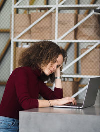 Young serious female and typing on keyboard of modern laptop while sitting at table in stylish cafe.