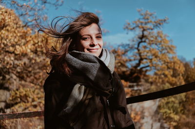 Portrait of smiling young woman wearing warm clothing while standing in forest during autumn