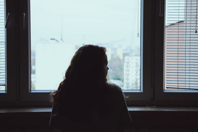 Rear view of woman looking through window at home