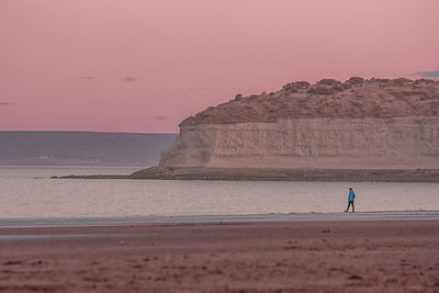 Man on rock by sea against sky during sunset