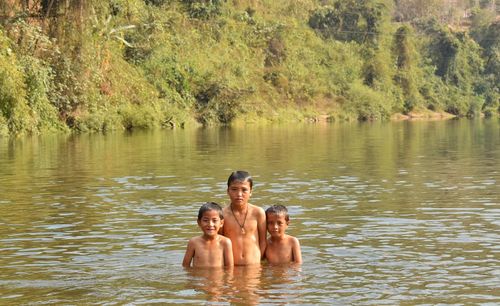 Portrait of shirtless brothers standing in lake against trees