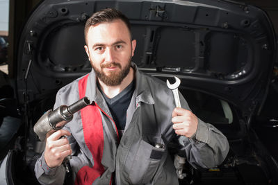 Portrait of male mechanic holding tools while sitting on chair