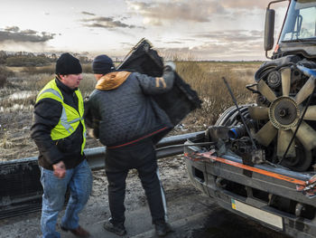 Mechanic with damaged truck on road during sunset